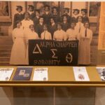 Alpha Chi Sigma sorority members posing with banner and memorabilia.