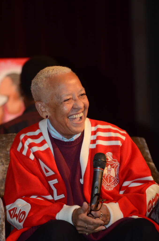 Smiling elderly person wrapped in a red and white blanket.