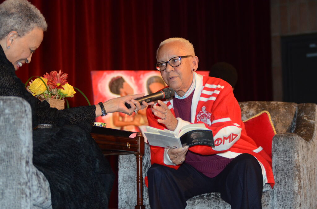 Man in glasses speaking into a microphone while reading from a book.