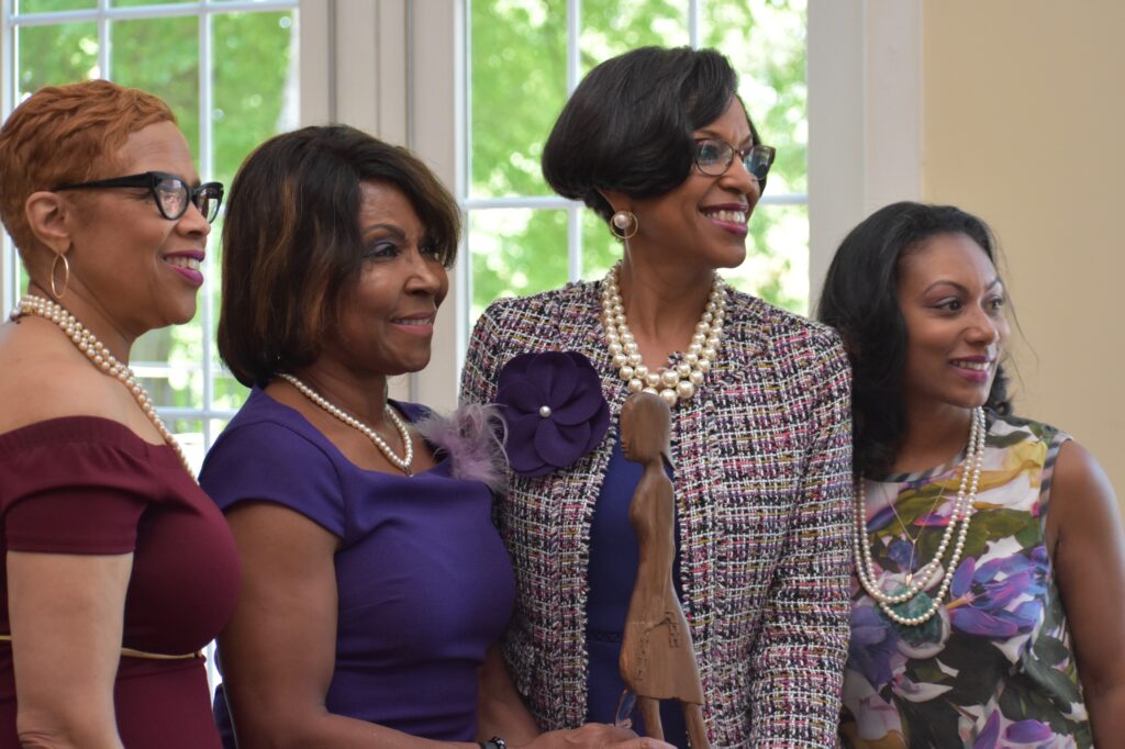 Three women standing together smiling in a bright room.