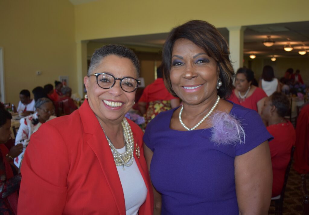 Two women smiling at a social event indoors.