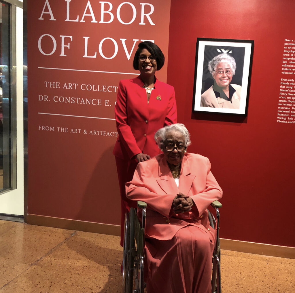 Two women pose in front of a museum exhibit titled 'A Labor of Love'.