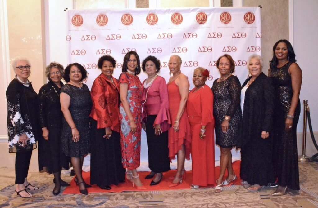 Group of well-dressed individuals posing at an event with a branded backdrop.