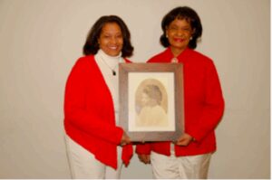 Two women in red cardigans holding a framed artwork.