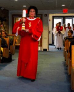 Woman in red choir robe holding a candle walking down aisle.