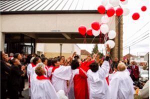 Children in white and red robes releasing red and white balloons outdoors.