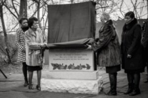 Two people unveiling a commemorative plaque outdoors in winter.