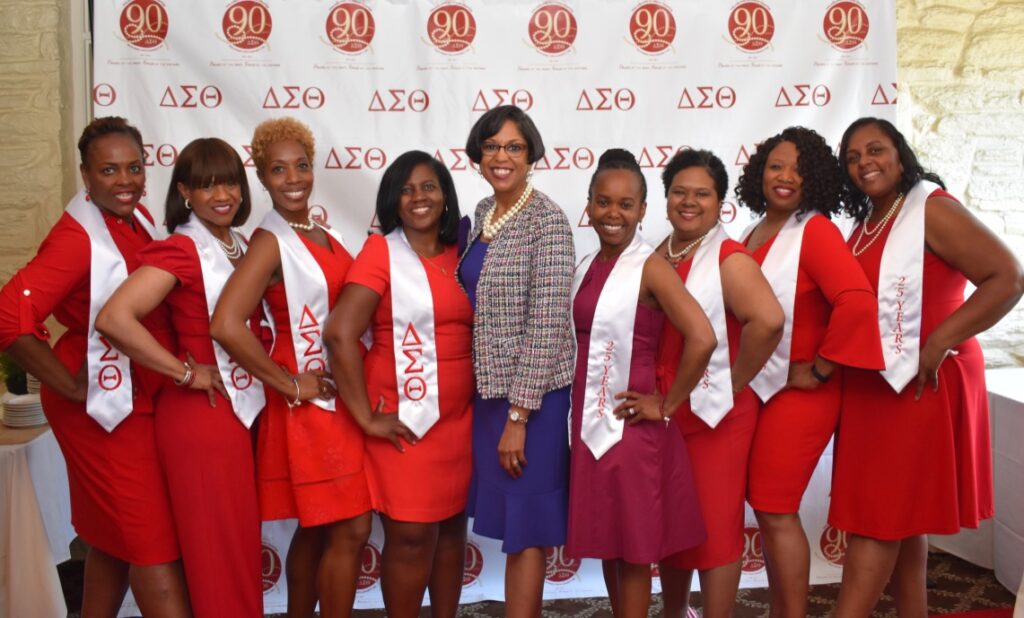 A group of women smiling in red and white attire at a Delta Sigma Theta event.