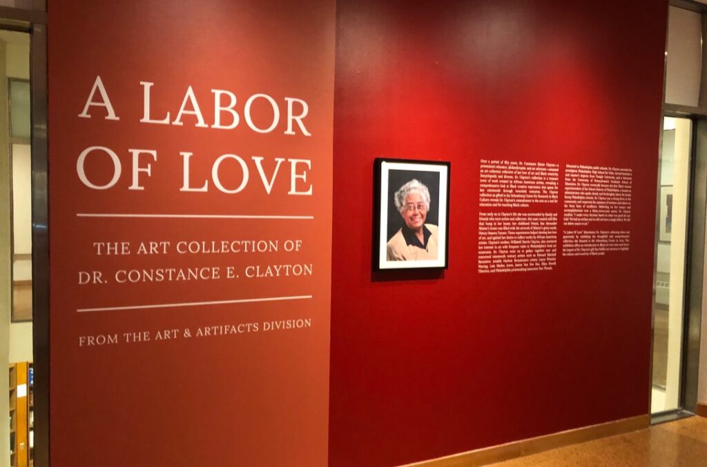 Exhibit entrance titled 'Labor of Love' with a portrait and descriptive text on a red wall.