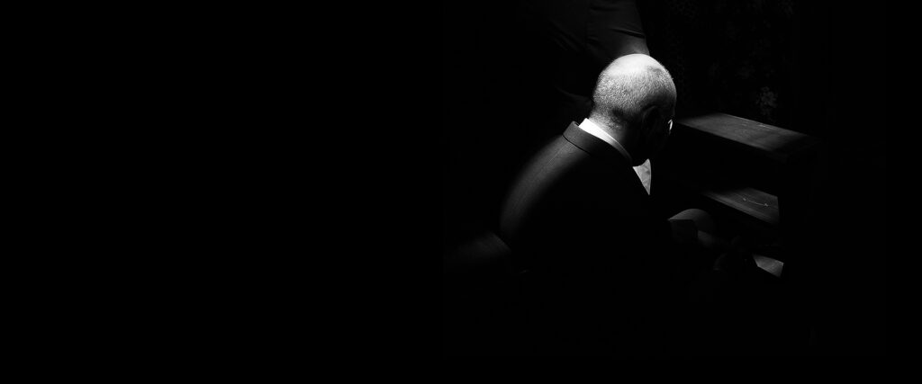 Black and white photo of a bald man in a suit walking into darkness.
