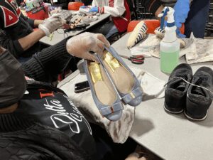A person holding a pair of silver and gold ballet flats with bows.