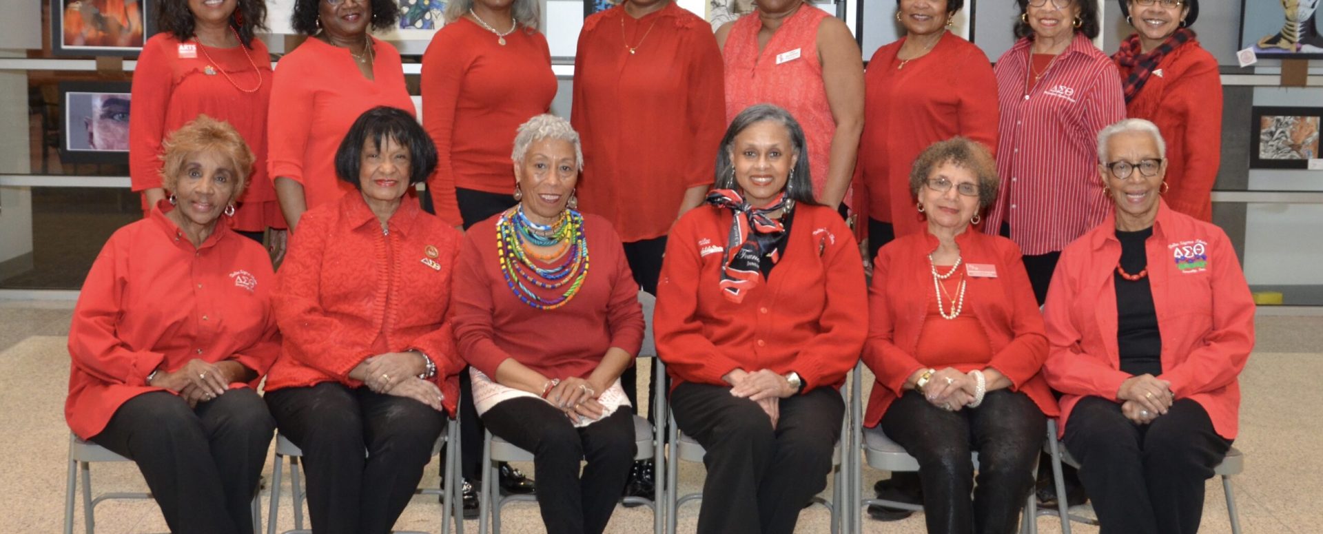 Group of women dressed in red posing indoors with framed photos behind them.
