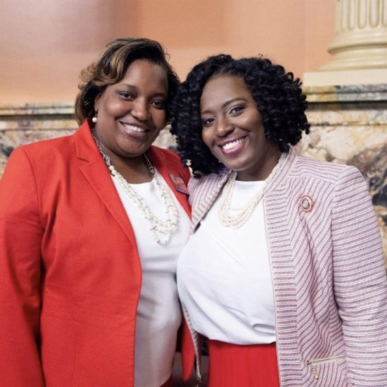 Two women smiling warmly, dressed in red and white attire.