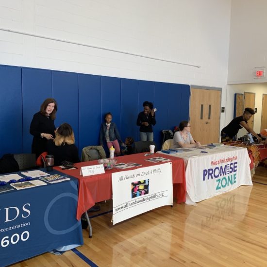 People at informational tables in a gymnasium for a community event.