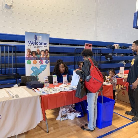 People at a community event booth in a gymnasium.