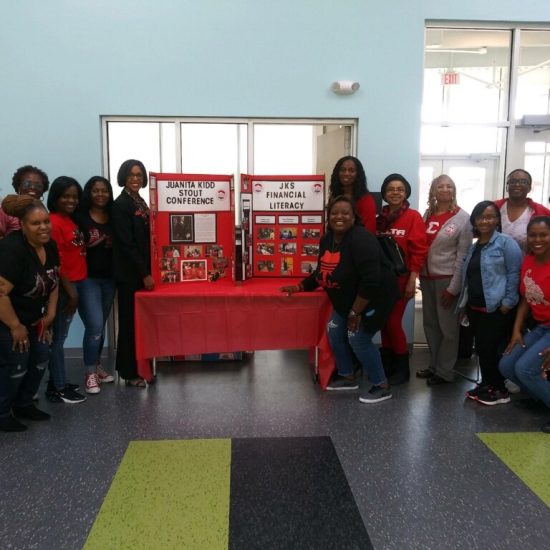 Group of people posing around a red-themed display table indoors.