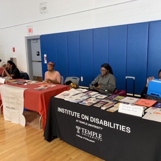 Two informational tables at an indoor event with people seated behind them.