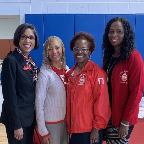 Four women standing together, smiling in a gymnasium.