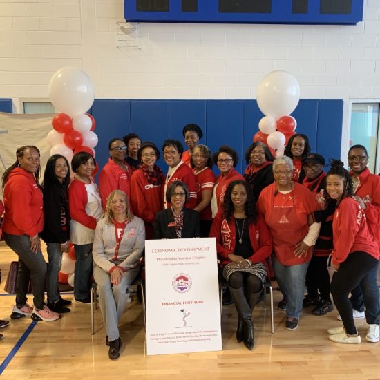 Group photo of people in red shirts at an indoor event with balloons and a sign.