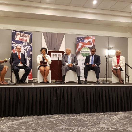 Four people seated on a stage panel during a discussion event.