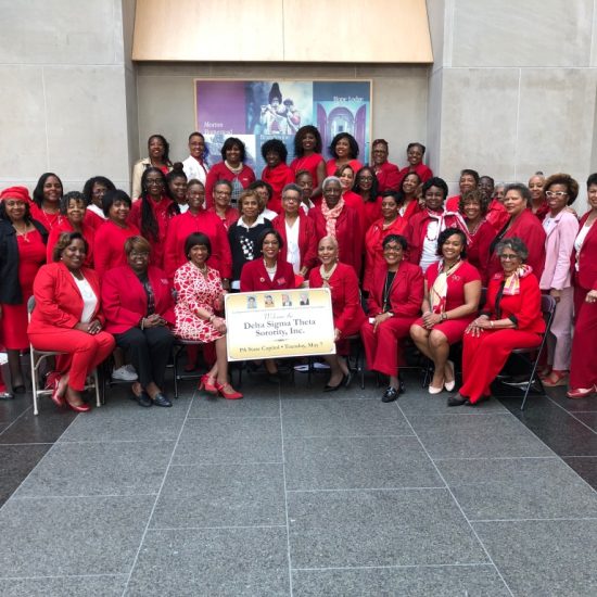 Group of people dressed in red posing with a sign outdoors.