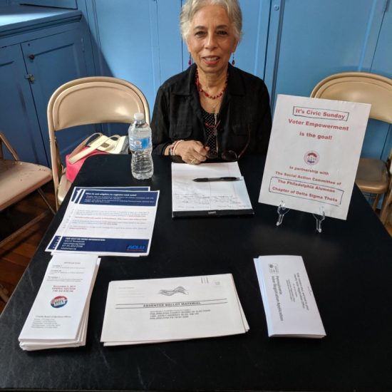 A woman at a table with informational pamphlets and a sign about volunteering.