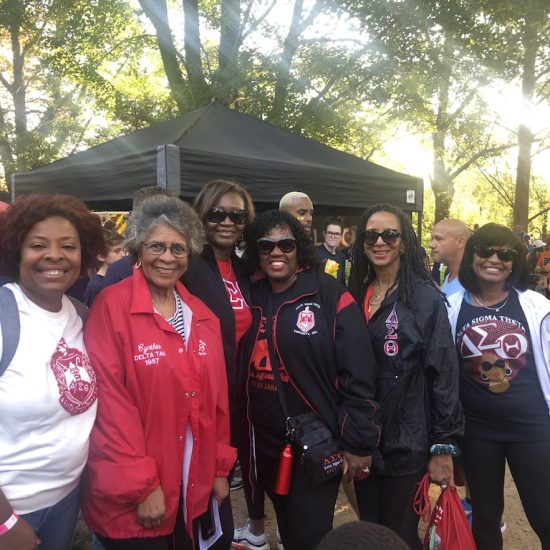 Group of women smiling outdoors, wearing matching jackets and shirts.