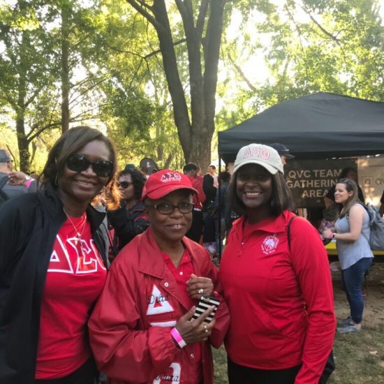 Four women in red and pink shirts posing outdoors at a daytime event.