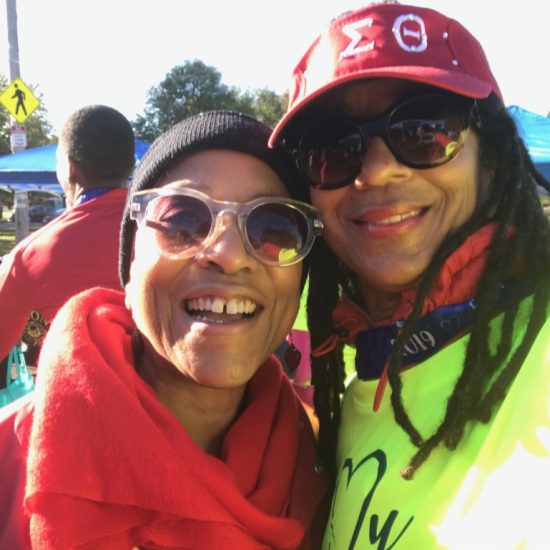 Two women smiling outdoors, one in red and the other in a neon yellow shirt and red cap.