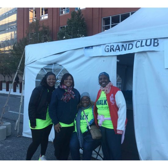 Group of four people posing cheerfully outside a Grand Club tent.