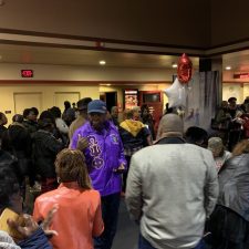 Crowded indoor event with people socializing and standing closely together.