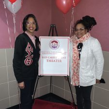 Two women standing beside a sign promoting breast cancer awareness.