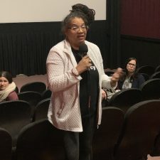 A woman speaking into a microphone in a theater.
