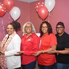Five women standing in a row holding red and white balloons.