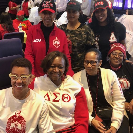 A group of women wearing Delta Sigma Theta sorority apparel pose together indoors.