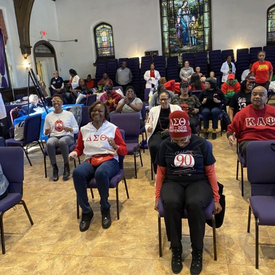 A group of people seated indoors wearing masks and red shirts.
