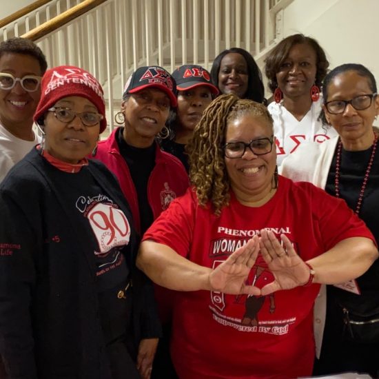 A group of women smiling and posing together indoors, wearing themed shirts and hats.