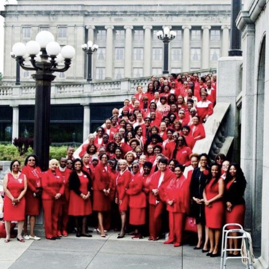 Large group of people dressed in red posing on stairs outside a building.